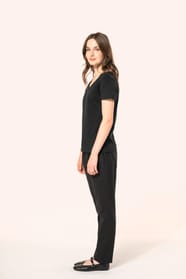 Jeune femme aux cheveux châtains longs et légèrement ondulés portant un T-shirt noir à manches courtes en coton Supima® col V, coupe droite, 180 g/m². Sa fibre extra-longue apporte résistance et douceur, tandis que les finitions soignées et la constructio