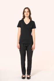 Jeune femme aux cheveux châtains longs et légèrement ondulés portant un T-shirt noir à manches courtes en coton Supima® col V, coupe droite, 180 g/m². Sa fibre extra-longue apporte résistance et douceur, tandis que les finitions soignées et la constructio