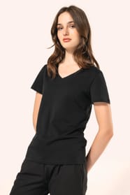 Jeune femme aux cheveux châtains longs et légèrement ondulés portant un T-shirt noir à manches courtes en coton Supima® col V, coupe droite, 180 g/m². Sa fibre extra-longue apporte résistance et douceur, tandis que les finitions soignées et la constructio