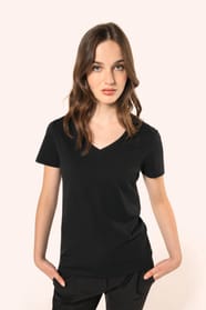 Jeune femme aux cheveux châtains longs et légèrement ondulés portant un T-shirt noir à manches courtes en coton Supima® col V, coupe droite, 180 g/m². Sa fibre extra-longue apporte résistance et douceur, tandis que les finitions soignées et la constructio