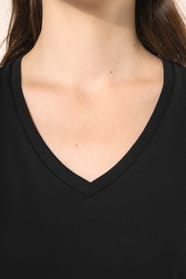 Jeune femme aux cheveux châtains longs et légèrement ondulés portant un T-shirt noir à manches courtes en coton Supima® col V, coupe droite, 180 g/m². Sa fibre extra-longue apporte résistance et douceur, tandis que les finitions soignées et la constructio