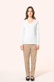 Jeune femme aux cheveux châtains longs et légèrement ondulés portant un T-shirt blanc à manches longues en coton Supima® col V, coupe droite, 180 g/m². Sa fibre extra-longue apporte résistance et douceur, tandis que les finitions soignées et la constructi