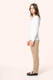 Jeune femme aux cheveux châtains longs et légèrement ondulés portant un T-shirt blanc à manches longues en coton Supima® col V, coupe droite, 180 g/m². Sa fibre extra-longue apporte résistance et douceur, tandis que les finitions soignées et la constructi