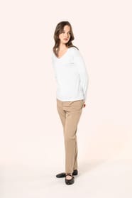 Jeune femme aux cheveux châtains longs et légèrement ondulés portant un T-shirt blanc à manches longues en coton Supima® col V, coupe droite, 180 g/m². Sa fibre extra-longue apporte résistance et douceur, tandis que les finitions soignées et la constructi