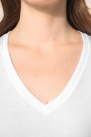 Jeune femme aux cheveux châtains longs et légèrement ondulés portant un T-shirt blanc à manches longues en coton Supima® col V, coupe droite, 180 g/m². Sa fibre extra-longue apporte résistance et douceur, tandis que les finitions soignées et la constructi