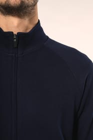 Jeune homme aux cheveux châtains courts portant une veste zippée bleu marine, coupe contemporaine et confortable, 320 g/m². Son tissu bénéficie du traitement LSI (Low Shrinkage Interlock) qui garantit un faible rétrécissement. Il complète sa tenue avec un