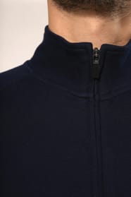 Jeune homme aux cheveux châtains courts portant une veste zippée bleu marine, coupe contemporaine et confortable, 320 g/m². Son tissu bénéficie du traitement LSI (Low Shrinkage Interlock) qui garantit un faible rétrécissement. Il complète sa tenue avec un