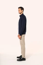 Jeune homme aux cheveux châtains courts portant une veste zippée bleu marine, coupe contemporaine et confortable, 320 g/m². Son tissu bénéficie du traitement LSI (Low Shrinkage Interlock) qui garantit un faible rétrécissement. Il complète sa tenue avec un