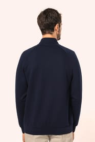 Jeune homme aux cheveux châtains courts portant une veste zippée bleu marine, coupe contemporaine et confortable, 320 g/m². Son tissu bénéficie du traitement LSI (Low Shrinkage Interlock) qui garantit un faible rétrécissement. Il complète sa tenue avec un