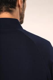 Jeune homme aux cheveux châtains courts portant une veste zippée bleu marine, coupe contemporaine et confortable, 320 g/m². Son tissu bénéficie du traitement LSI (Low Shrinkage Interlock) qui garantit un faible rétrécissement. Il complète sa tenue avec un
