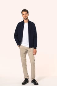 Jeune homme aux cheveux châtains courts portant une veste zippée bleu marine, coupe contemporaine et confortable, 320 g/m². Son tissu bénéficie du traitement LSI (Low Shrinkage Interlock) qui garantit un faible rétrécissement. Il complète sa tenue avec un