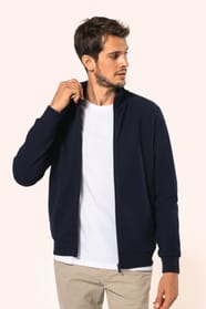 Jeune homme aux cheveux châtains courts portant une veste zippée bleu marine, coupe contemporaine et confortable, 320 g/m². Son tissu bénéficie du traitement LSI (Low Shrinkage Interlock) qui garantit un faible rétrécissement. Il complète sa tenue avec un