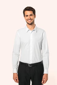 Jeune homme aux cheveux châtains courts portant une chemise blanche en popeline à manches longues, dotée d’un col avec baleines amovibles. Les hirondelles de renfort, petits triangles de tissu reliant les pans avant et arrière, soulignent la précision d’u