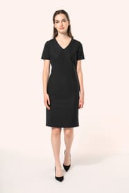 Jeune femme aux cheveux châtains longs attachés en demi-queue portant une robe noire à la coupe cintrée et élégante. Ses finitions soignées apportent classe et sobriété, tandis que son encolure en V avec finition intérieure doublée souligne le raffinement