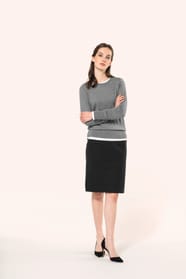 Jeune femme aux cheveux châtains attachés en demi-queue portant une jupe droite confectionnée dans un mélange de matières de qualité (50% polyester, 23% viscose, 22% laine, 5% élasthanne) avec doublure stretch 100% polyester. Son confort est renforcé par 