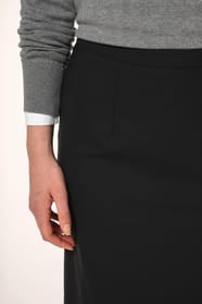 Jeune femme aux cheveux châtains attachés en demi-queue portant une jupe droite confectionnée dans un mélange de matières de qualité (50% polyester, 23% viscose, 22% laine, 5% élasthanne) avec doublure stretch 100% polyester. Son confort est renforcé par 