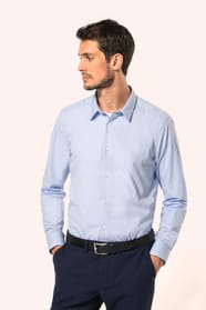 Jeune homme aux cheveux châtains courts portant une chemise bleu clair en popeline à manches longues, confectionnée en coton peigné double retors 80x2 pour une qualité supérieure. Sa coupe ajustée est structurée par deux pinces dans le dos, tandis que les