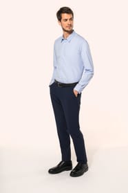 Jeune homme aux cheveux châtains courts portant une chemise bleu clair en popeline à manches longues, confectionnée en coton peigné double retors 80x2 pour une qualité supérieure. Sa coupe ajustée est structurée par deux pinces dans le dos, tandis que les
