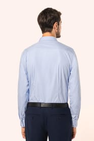 Jeune homme aux cheveux châtains courts portant une chemise bleu clair en popeline à manches longues, confectionnée en coton peigné double retors 80x2 pour une qualité supérieure. Sa coupe ajustée est structurée par deux pinces dans le dos, tandis que les