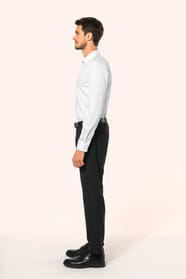 Jeune homme aux cheveux châtains courts portant une chemise blanche en twill à manches longues, confectionnée en coton double retors 80x2 de qualité supérieure. Sa coupe ajustée, structurée par deux pinces dans le dos, se distingue par des finitions raffi