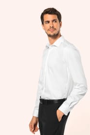 Jeune homme aux cheveux châtains courts portant une chemise blanche en twill à manches longues, confectionnée en coton double retors 80x2 de qualité supérieure. Sa coupe ajustée, structurée par deux pinces dans le dos, se distingue par des finitions raffi