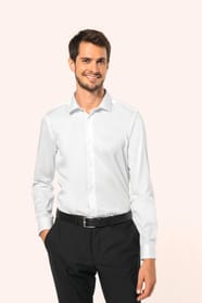 Jeune homme aux cheveux châtains courts portant une chemise blanche en twill à manches longues, confectionnée en coton double retors 80x2 de qualité supérieure. Sa coupe ajustée, structurée par deux pinces dans le dos, se distingue par des finitions raffi