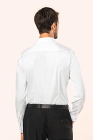 Jeune homme aux cheveux châtains courts portant une chemise blanche en twill à manches longues, confectionnée en coton double retors 80x2 de qualité supérieure. Sa coupe ajustée, structurée par deux pinces dans le dos, se distingue par des finitions raffi