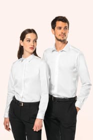 Jeune femme aux cheveux châtains longs attachés en demi-queue et jeune homme aux cheveux châtains courts portent une chemise blanche en twill à manches longues, confectionnée en coton double retors 80x2 de qualité supérieure. Leur coupe ajustée est sublim