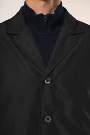 Jeune homme aux cheveux châtains courts portant un trench structuré noir à col tailleur, alliant élégance et sobriété. Confectionné en polyester trois couches contrecollées, il associe technicité et confort grâce à un tissu imperméable 8000 mm et un rembo