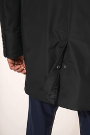 Jeune homme aux cheveux châtains courts portant un trench structuré noir à col tailleur, alliant élégance et sobriété. Confectionné en polyester trois couches contrecollées, il associe technicité et confort grâce à un tissu imperméable 8000 mm et un rembo