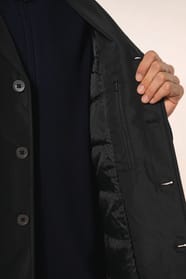 Jeune homme aux cheveux châtains courts portant un trench structuré noir à col tailleur, alliant élégance et sobriété. Confectionné en polyester trois couches contrecollées, il associe technicité et confort grâce à un tissu imperméable 8000 mm et un rembo