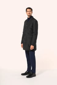 Jeune homme aux cheveux châtains courts portant un trench structuré noir à col tailleur, alliant élégance et sobriété. Confectionné en polyester trois couches contrecollées, il associe technicité et confort grâce à un tissu imperméable 8000 mm et un rembo