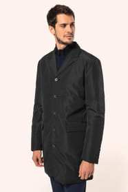 Jeune homme aux cheveux châtains courts portant un trench structuré noir à col tailleur, alliant élégance et sobriété. Confectionné en polyester trois couches contrecollées, il associe technicité et confort grâce à un tissu imperméable 8000 mm et un rembo