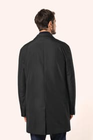 Jeune homme aux cheveux châtains courts portant un trench structuré noir à col tailleur, alliant élégance et sobriété. Confectionné en polyester trois couches contrecollées, il associe technicité et confort grâce à un tissu imperméable 8000 mm et un rembo