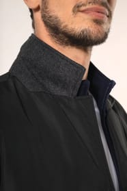 Jeune homme aux cheveux châtains courts portant un trench structuré noir à col tailleur, ouvert sur un T-shirt blanc rentré dans un pantalon de costume bleu, maintenu par une ceinture marron. Confectionné en polyester trois couches contrecollées, il assoc