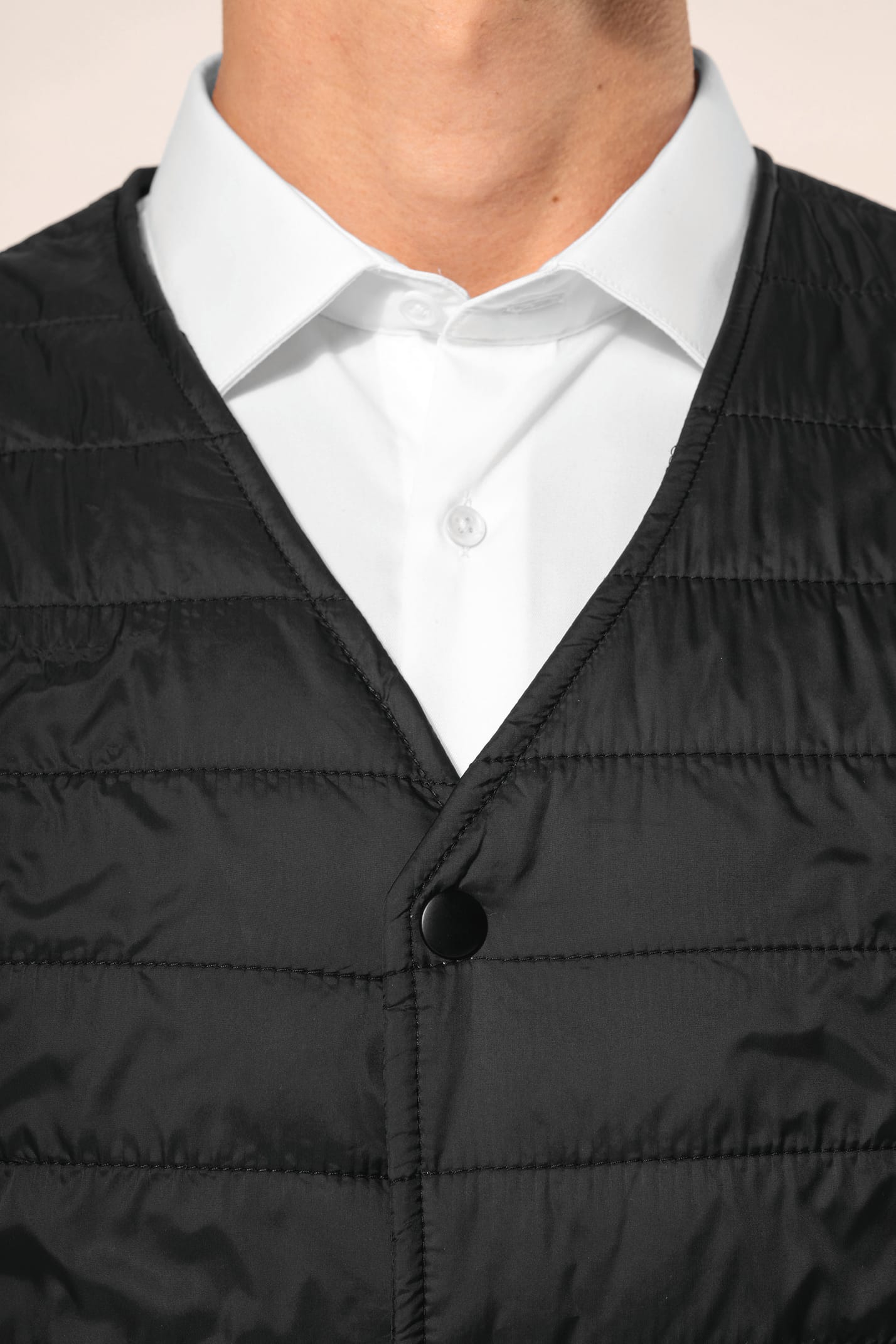 Jeune homme aux cheveux châtains courts portant un bodywarmer léger noir, conçu pour être porté seul ou sous une veste grâce à sa finesse. Réalisé en polyamide avec un rembourrage intérieur en Thinsulate™, il assure un maintien optimal de la chaleur tout 
