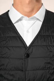 Jeune homme aux cheveux châtains courts portant un bodywarmer léger noir, conçu pour être porté seul ou sous une veste grâce à sa finesse. Réalisé en polyamide avec un rembourrage intérieur en Thinsulate™, il assure un maintien optimal de la chaleur tout 