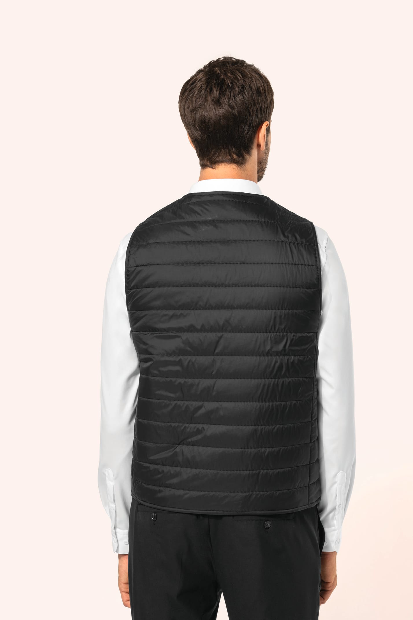 Jeune homme aux cheveux châtains courts portant un bodywarmer léger noir, conçu pour être porté seul ou sous une veste grâce à sa finesse. Réalisé en polyamide avec un rembourrage intérieur en Thinsulate™, il assure un maintien optimal de la chaleur tout 