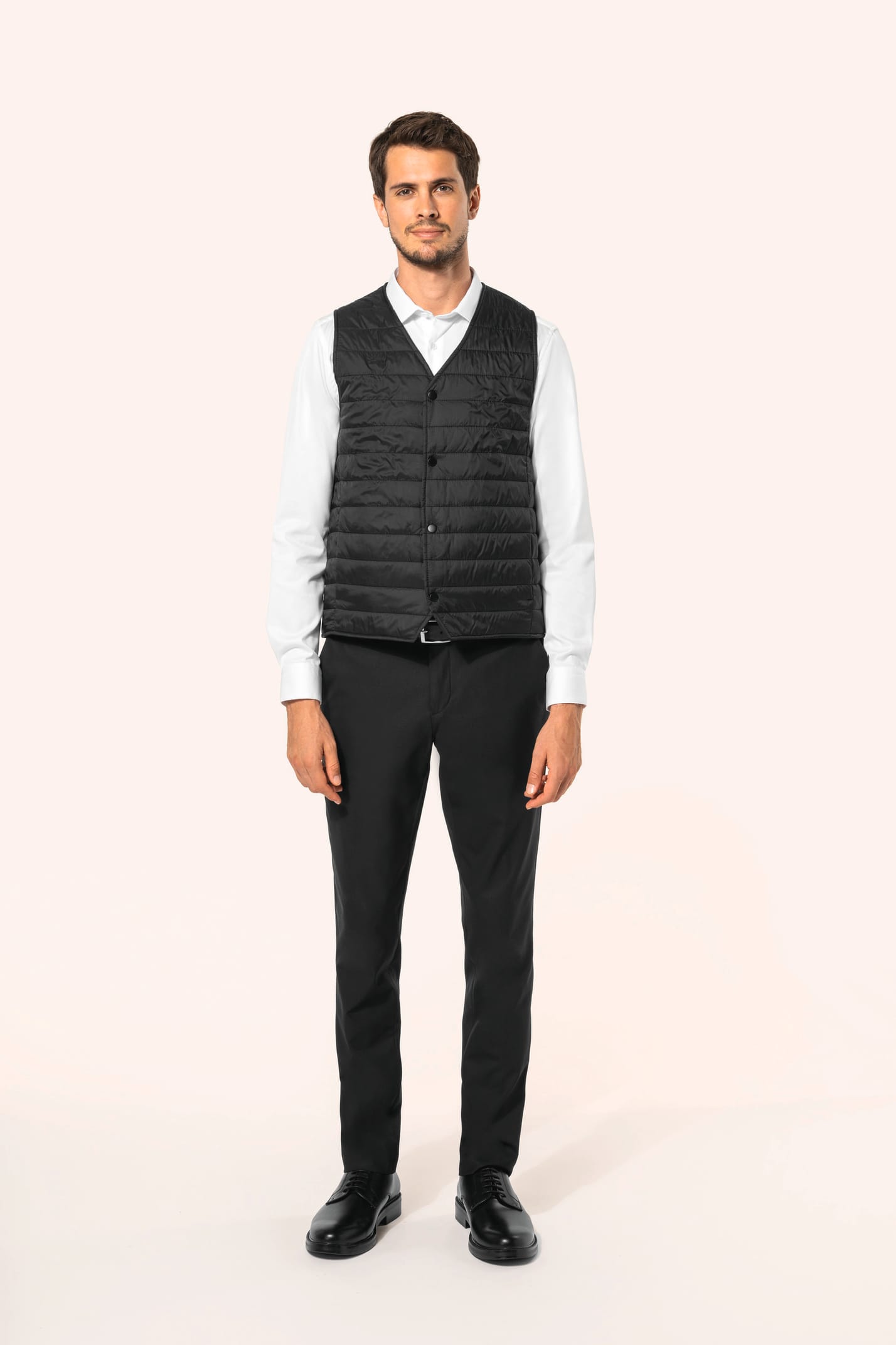 Jeune homme aux cheveux châtains courts portant un bodywarmer léger noir, conçu pour être porté seul ou sous une veste grâce à sa finesse. Réalisé en polyamide avec un rembourrage intérieur en Thinsulate™, il assure un maintien optimal de la chaleur tout 
