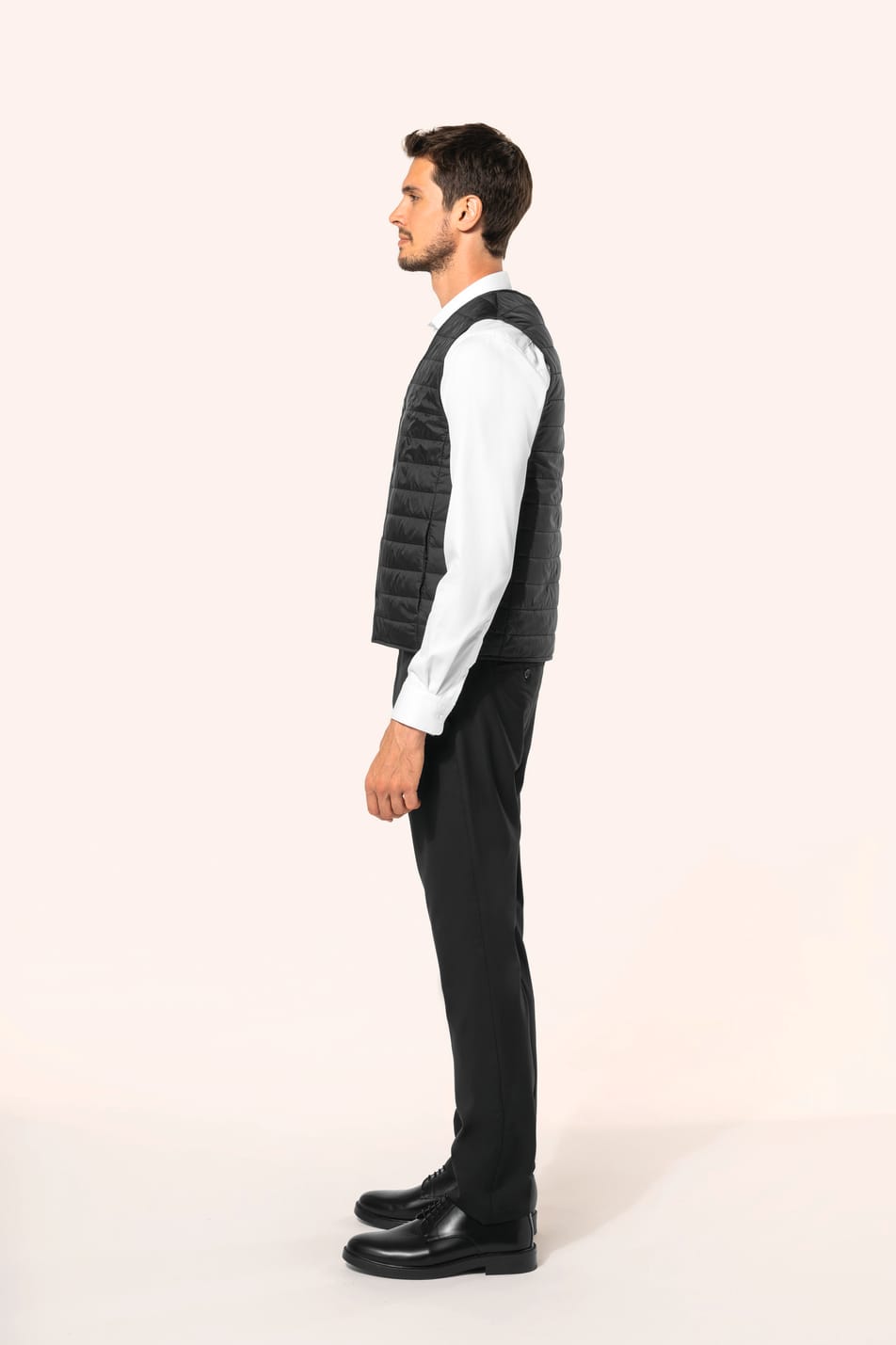 Jeune homme aux cheveux châtains courts portant un bodywarmer léger noir, conçu pour être porté seul ou sous une veste grâce à sa finesse. Réalisé en polyamide avec un rembourrage intérieur en Thinsulate™, il assure un maintien optimal de la chaleur tout 