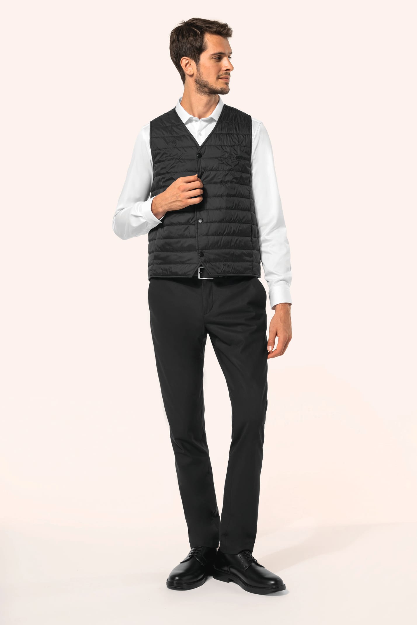 Jeune homme aux cheveux châtains courts portant un bodywarmer léger noir, conçu pour être porté seul ou sous une veste grâce à sa finesse. Réalisé en polyamide avec un rembourrage intérieur en Thinsulate™, il assure un maintien optimal de la chaleur tout 