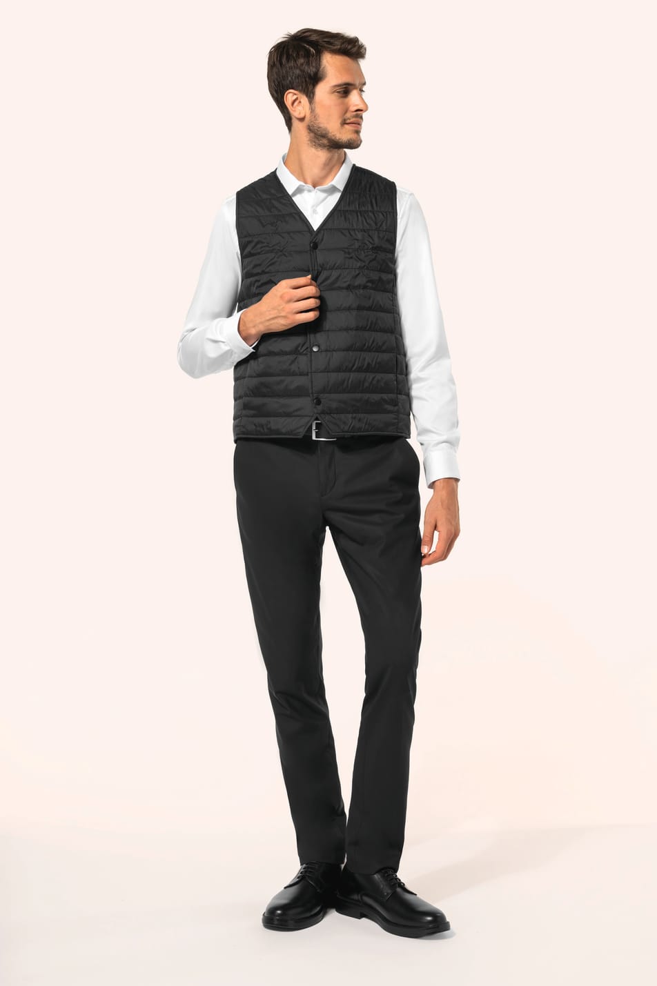 Jeune homme aux cheveux châtains courts portant un bodywarmer léger noir, conçu pour être porté seul ou sous une veste grâce à sa finesse. Réalisé en polyamide avec un rembourrage intérieur en Thinsulate™, il assure un maintien optimal de la chaleur tout 