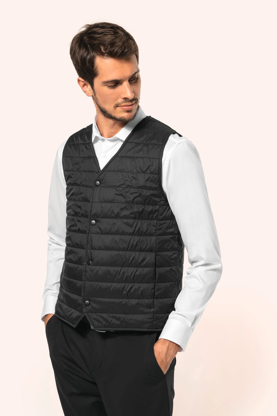 Jeune homme aux cheveux châtains courts portant un bodywarmer léger noir, conçu pour être porté seul ou sous une veste grâce à sa finesse. Réalisé en polyamide avec un rembourrage intérieur en Thinsulate™, il assure un maintien optimal de la chaleur tout 