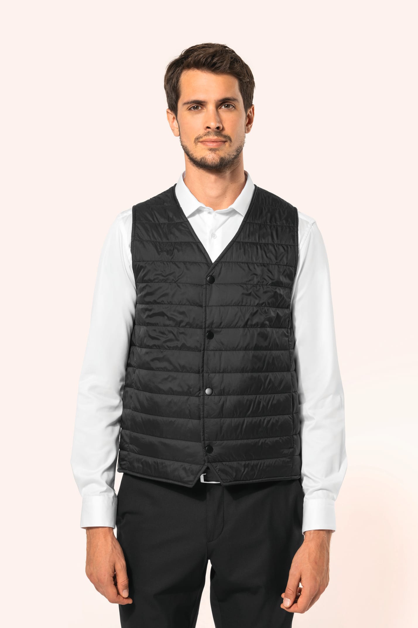 Jeune homme aux cheveux châtains courts portant un bodywarmer léger noir, conçu pour être porté seul ou sous une veste grâce à sa finesse. Réalisé en polyamide avec un rembourrage intérieur en Thinsulate™, il assure un maintien optimal de la chaleur tout 