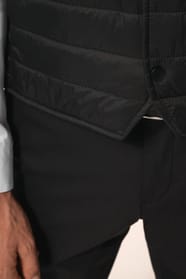 Jeune homme aux cheveux châtains courts portant un bodywarmer léger noir, conçu pour être porté seul ou sous une veste grâce à sa finesse. Réalisé en polyamide avec un rembourrage intérieur en Thinsulate™, il assure un maintien optimal de la chaleur tout 