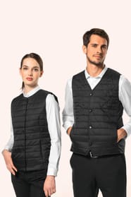 Jeune femme aux cheveux châtains longs attachés en queue de cheval et jeune homme aux cheveux châtains courts portent un bodywarmer léger noir, pensé pour se glisser aisément sous une veste. Confectionnés en polyamide avec un rembourrage intérieur en Thin