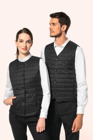 Jeune femme aux cheveux châtains longs attachés en queue de cheval et jeune homme aux cheveux châtains courts portent un bodywarmer léger noir, pensé pour se glisser aisément sous une veste. Confectionnés en polyamide avec un rembourrage intérieur en Thin