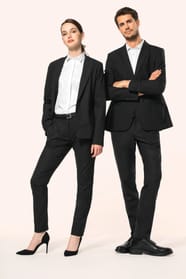 Jeune homme aux cheveux châtains courts et jeune femme aux cheveux châtains longs attachés en queue de cheval composent un duo élégant en noir et blanc. Ils portent chacun une veste noire à la coupe ajustée, associée à une chemise blanche, un pantalon noi