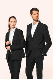 Jeune homme aux cheveux châtains courts et jeune femme aux cheveux châtains longs attachés en queue de cheval composent un duo élégant en noir et blanc. Ils portent chacun une veste noire à la coupe ajustée, associée à une chemise blanche, un pantalon noi