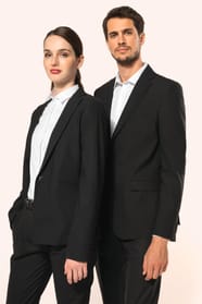 Jeune homme aux cheveux châtains courts et jeune femme aux cheveux châtains longs attachés en queue de cheval composent un duo élégant en noir et blanc. Ils portent chacun une veste noire à la coupe ajustée, associée à une chemise blanche, un pantalon noi